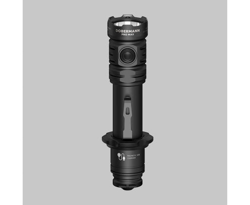 The Armytek Dobermann Pro Max tactical flashlight stands upright on a gray surface, highlighting its side switch and labeled magnetic USB charging port.