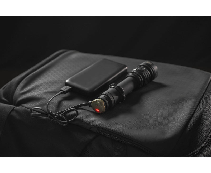 The Armytek Predator Pro Max tactical flashlight is connected to a portable power bank with a charging cable, both resting on a black bag.