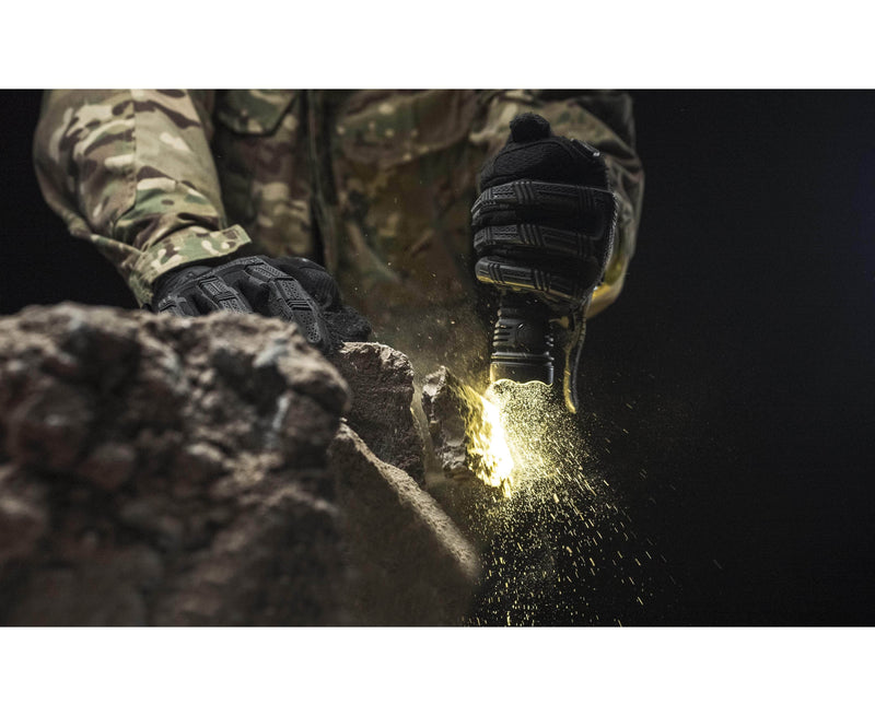 Wearing camo and gloves, a person uses the Armytek Predator Pro Max flashlight on rocky ground, making sparks fly.