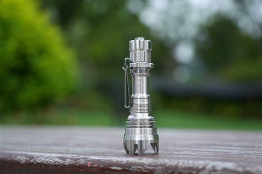 A Manker Striker Mini Titanium EDC Flashlight sitting on top of a wooden table.