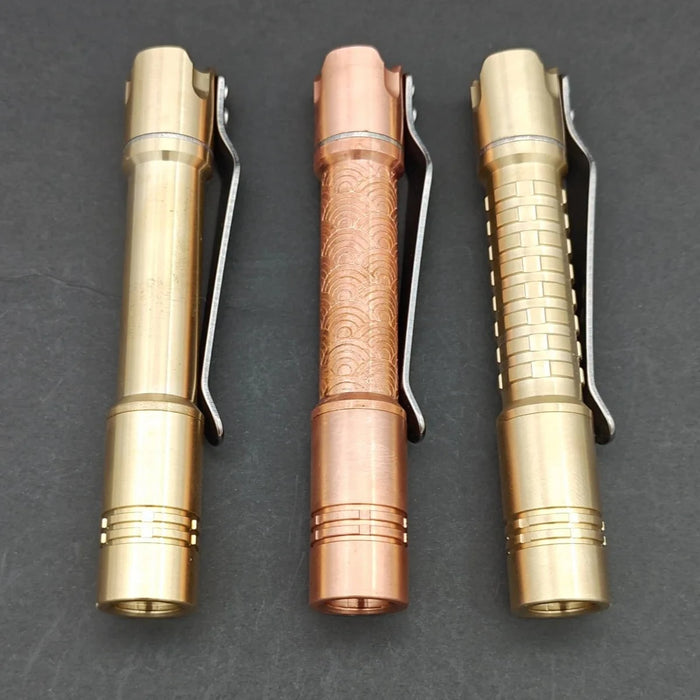 Three pen-shaped metal objects with pocket clips are displayed on a flat surface. The ReyLight Pineapple Mini MK II, featuring a rechargeable 10440 battery and Nichia 519a LED, showcases textures of smooth gold, patterned copper, and ridged gold.