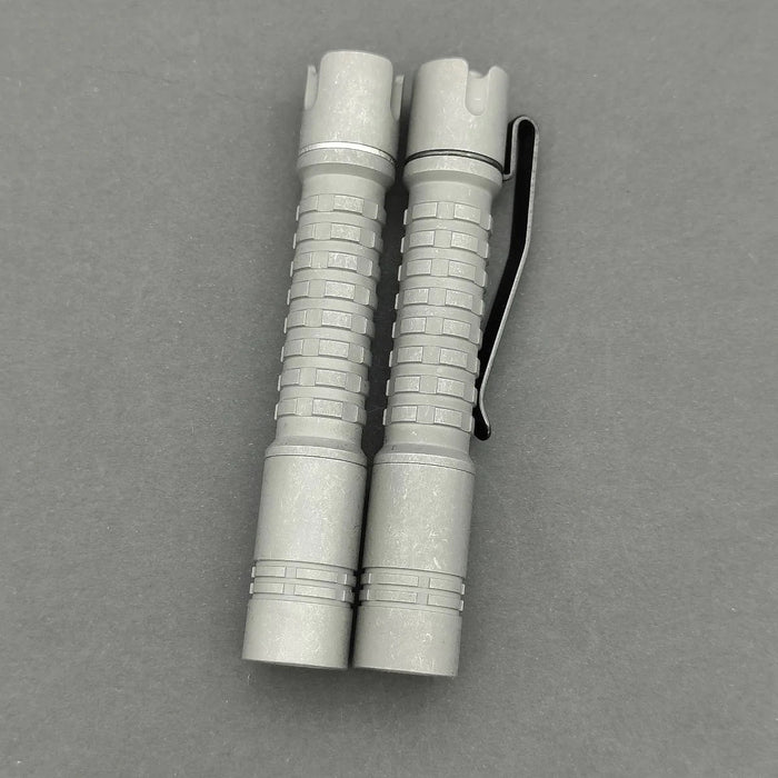 A pair of ReyLight Pineapple Mini Titanium flashlights on a gray surface, offering power and portability with 240 lumens.