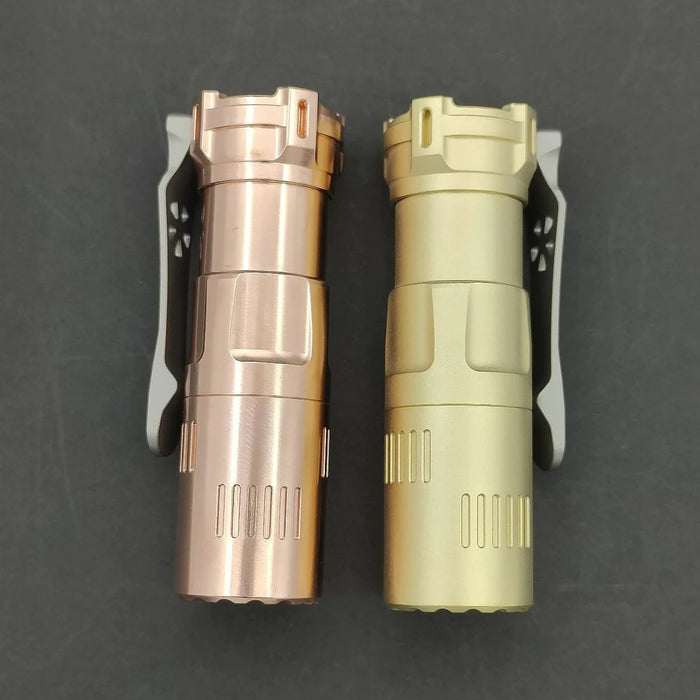 Two small flashlights, one copper and one brass, gleam side by side against a dark backdrop. Each ReyLight Rook features the Nichia 519a LED and a convenient, stylish clip on its side.