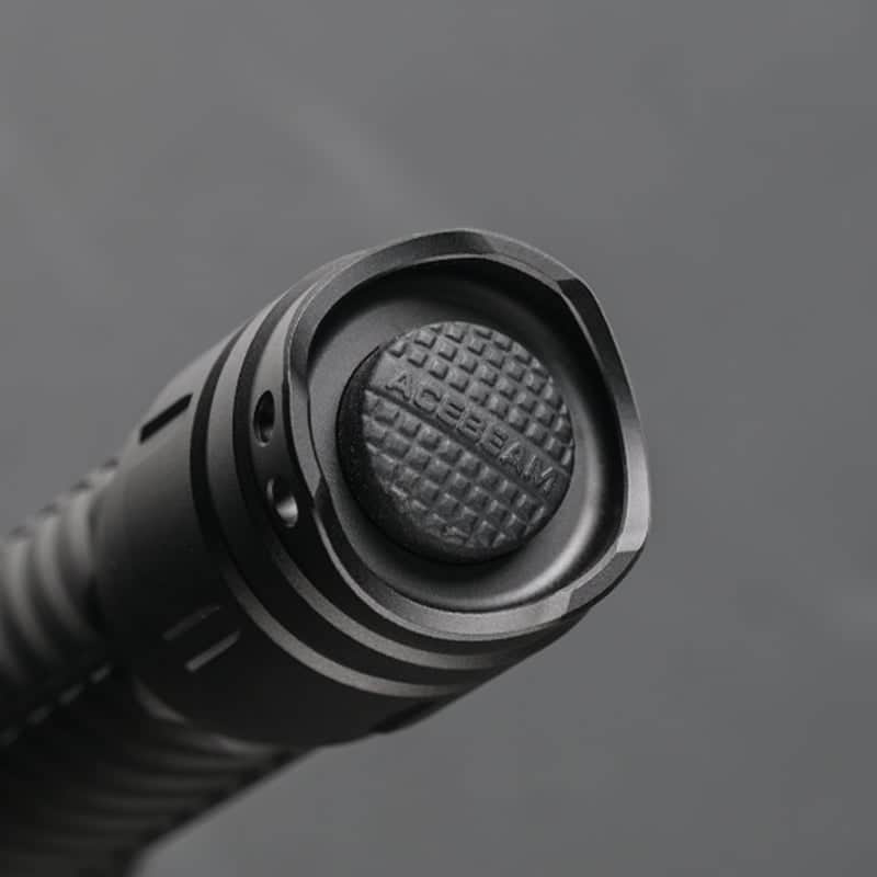 Close-up of the textured push button on the end of a black Acebeam T29 Ultra Long Range Hunting Flashlight against a gray background.