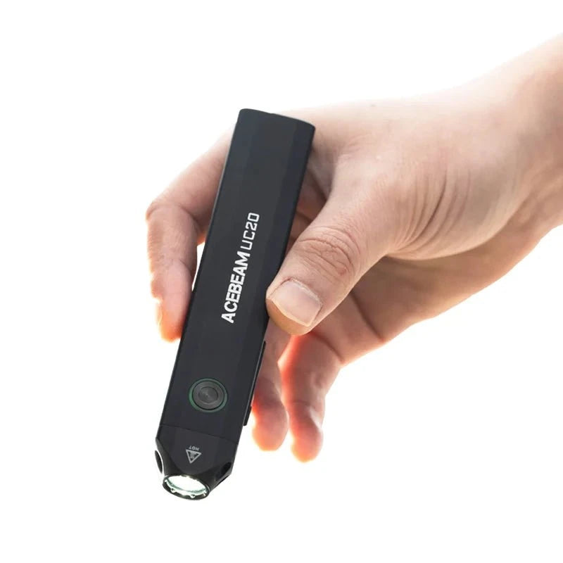 A hand displays the Acebeam UC20 flashlight, emphasizing its sleek design as a bright beam illuminates the front, showcasing its multifunctional versatility.