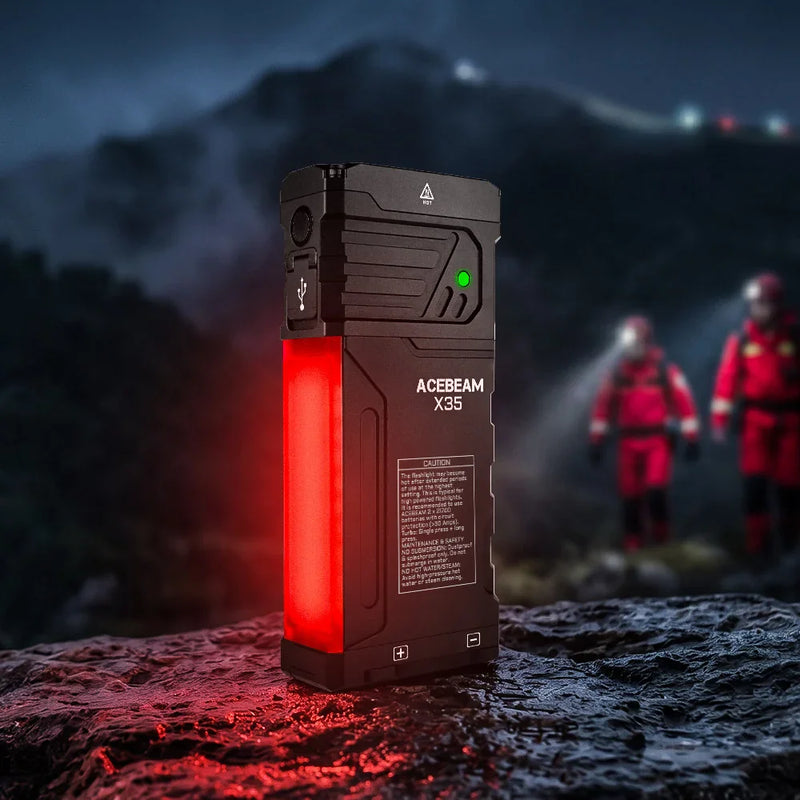 The Acebeam X35 Multi-Light Powerful Searching Flashlight with a glowing red panel rests on a wet rock at night, casting intense illumination ideal for emergency preparedness, while blurred rescue workers and mountains appear in the background.