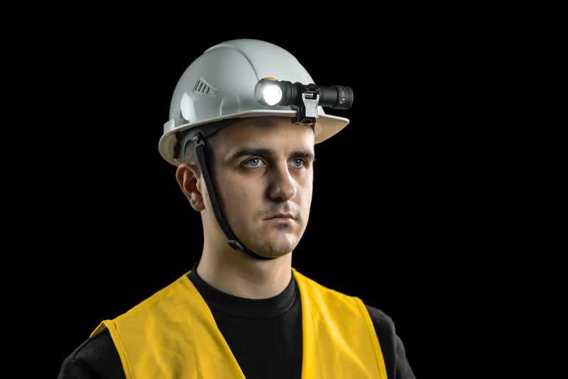 A man stands against a black background, wearing a white hard hat equipped with the Armytek Hard Hat Mount AHM-04 hands-free headlamp and a yellow safety vest.