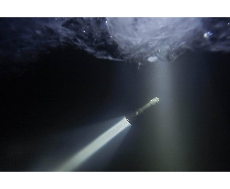 An Armytek Barracuda Pro Max Magnet USB flashlight beams upward through dark water, illuminating the icy surface above.