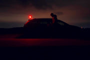 A person stands beside a parked car at night, illuminated by the Armytek Bear WRG warning light on the car roof and the subtle glow of its red and green flood lighting.