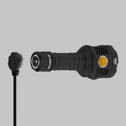 The Armytek Bear WRG, a black long-range flashlight featuring a yellow power button, is pictured with its detachable magnetic charging cable against a plain grey background. This rechargeable flashlight offers both durability and convenience for extended use.