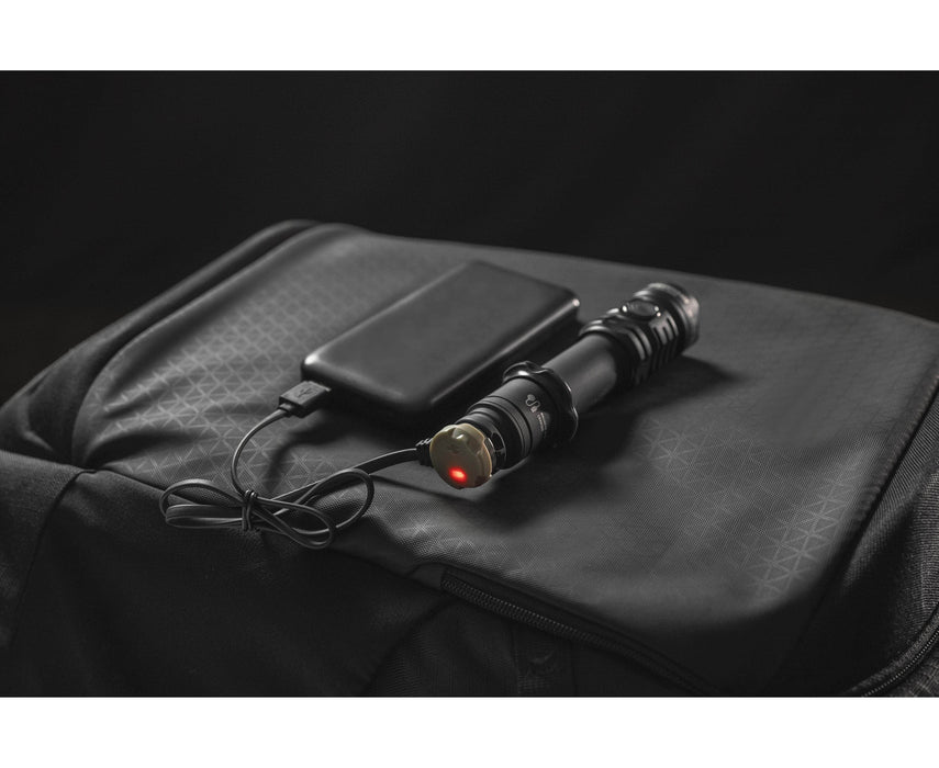 An Armytek Dobermann Pro Max is charging via USB from a power bank, both placed on a black textured bag.