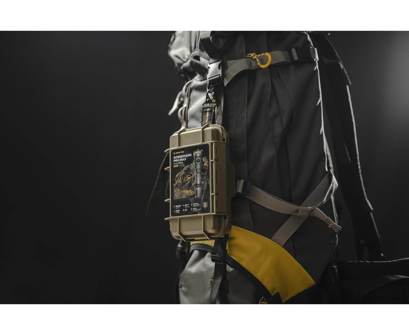 A compact Armytek Dobermann Pro Max tactical flashlight is attached to the strap of a large black and yellow backpack with a rugged olive green case and label, set against a dark background.