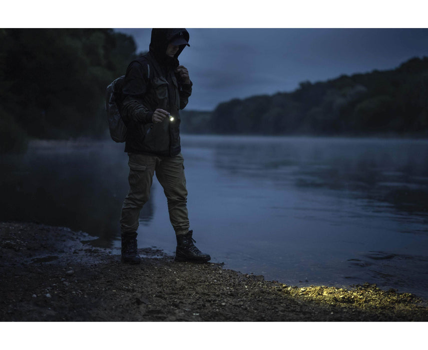 A man standing on the shore of a river at night, holding the Armytek Prime C1 Pro Magnet USB.