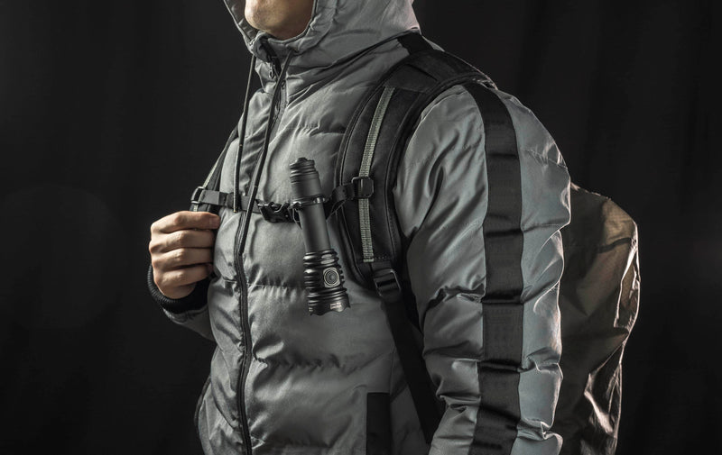 A person wears a gray hooded jacket and backpack with an Armytek Viking Pro Max Magnet USB - White flashlight attached to the chest strap, set against a dark background.