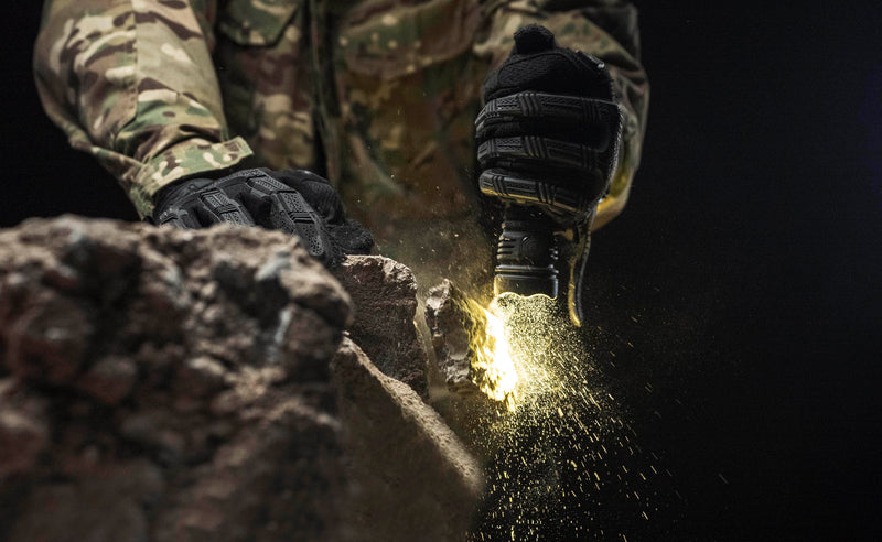 In the dark, someone in camouflage and tactical gloves sparks a flint on a rock as their Armytek Viking Pro Max Magnet USB - White flashlight rests nearby, ready for use.
