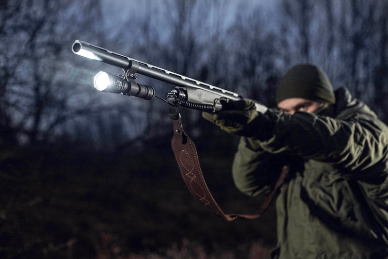 A person in outdoor gear points the Armytek Viking Pro Max Magnet USB - White flashlight in a dimly lit, wooded area.