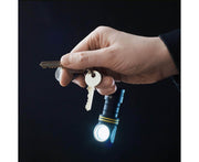 A hand holding a set of keys with the Armytek Elf C1 USB-C White flashlight attached, shining its brilliant 1000 lumens in the dark background, easily rechargeable via USB-C charger.