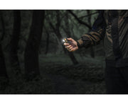 In a dense forest, a person stands with an Armytek Elf C1 USB-C White flashlight in hand, its 1000 lumens cutting through the dark surroundings.