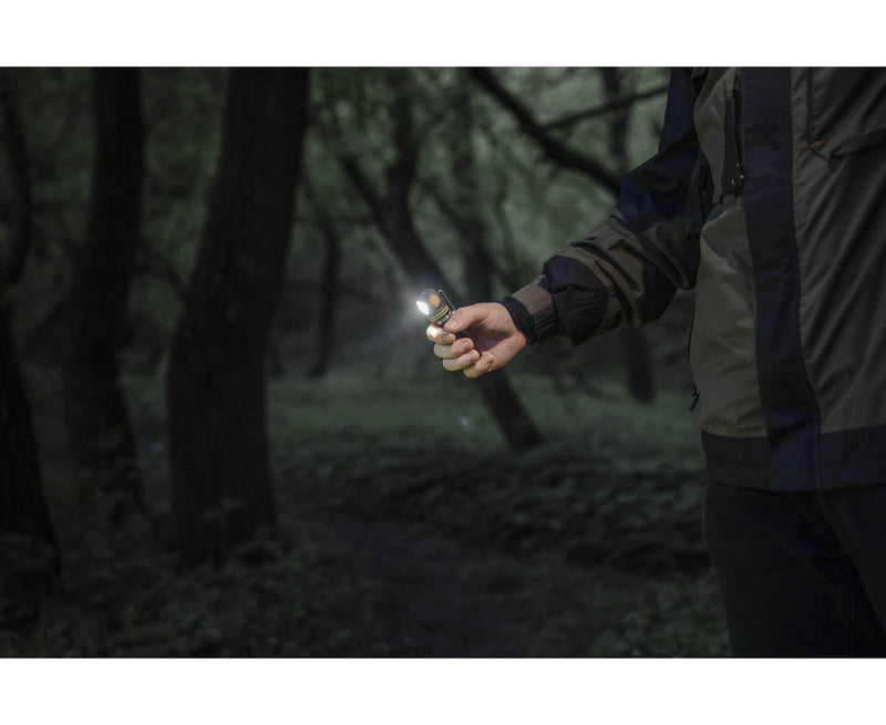 In a dark, wooded area, a person holds the Armytek Elf C2 USB-C Warm, its 1023 lumens piercing through the shadows. This multifunctional model ensures reliability and ease of use.