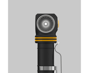 Close-up of an Armytek Elf C2 USB-C Warm flashlight, featuring a black casing with a warm yellow ring and textured lens, positioned upright against a plain gray background and offering convenient USB-C charging.