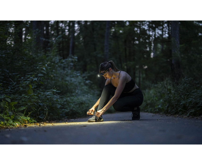 A woman, equipped with the Armytek Wizard C2 Pro Max LR - Warm headlamp, is tying her shoes in the warm woods at night.