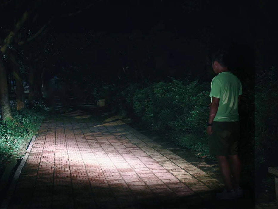 A man standing on a dimly lit path, holding a Fenix E18R flashlight for improved visibility.