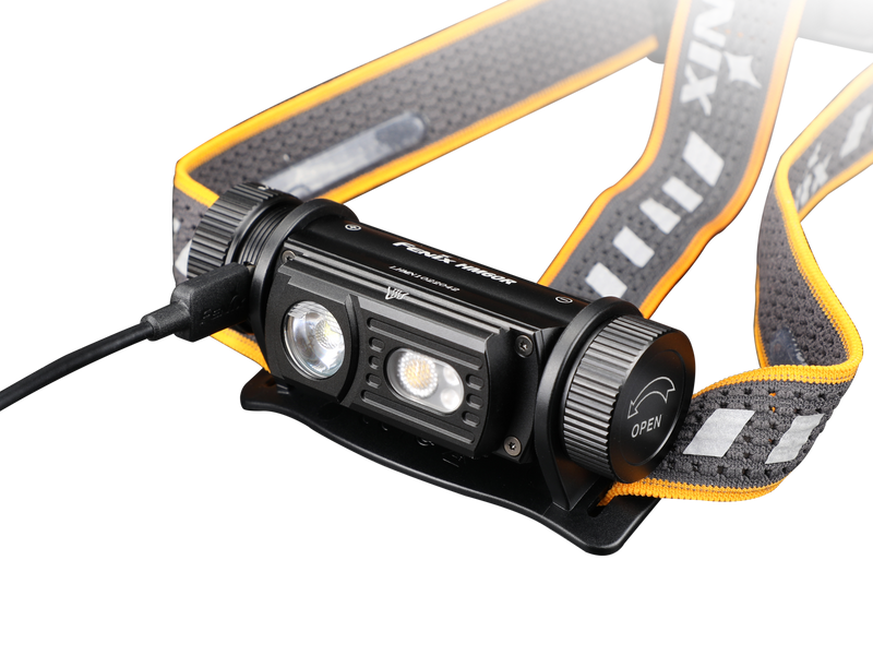 The Fenix HM60R is an outdoor headlamp in black and orange, equipped with a strap and two LED lights capable of delivering up to 1300 lumens. An additional cable connects to the side, enhancing its functionality.