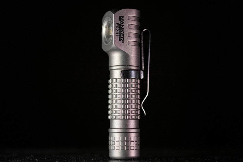 The compact Manker E02 III - Titanium flashlight stands upright against a black background, delivering 560 lumens—ideal for everyday carry.
