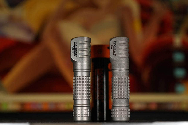 Two silver Manker E02 III - Titanium Everyday Carry Flashlights stand upright side by side with a battery between them against a blurred, colorful background—each offers brilliant 560-lumen illumination.