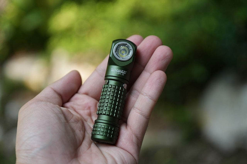 A hand holding the Manker E03H III, a small, green everyday carry flashlight with a textured grip, capable of emitting 1200 lumens.