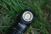 Close-up of the Manker E03H III everyday carry flashlight placed on grass, showcasing the LED light and branding on the head, boasting a powerful 1200 lumens output.
