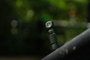 Close-up of the Manker E03H III, a small black flashlight standing vertically on a surface against a blurred green outdoor backdrop, perfect for an everyday carry setup.