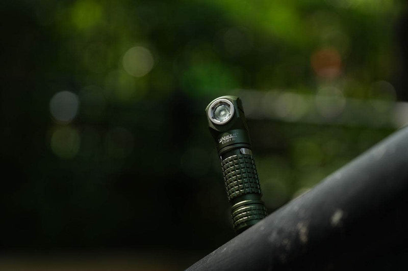 Close-up of the Manker E03H III, a small black flashlight standing vertically on a surface against a blurred green outdoor backdrop, perfect for an everyday carry setup.