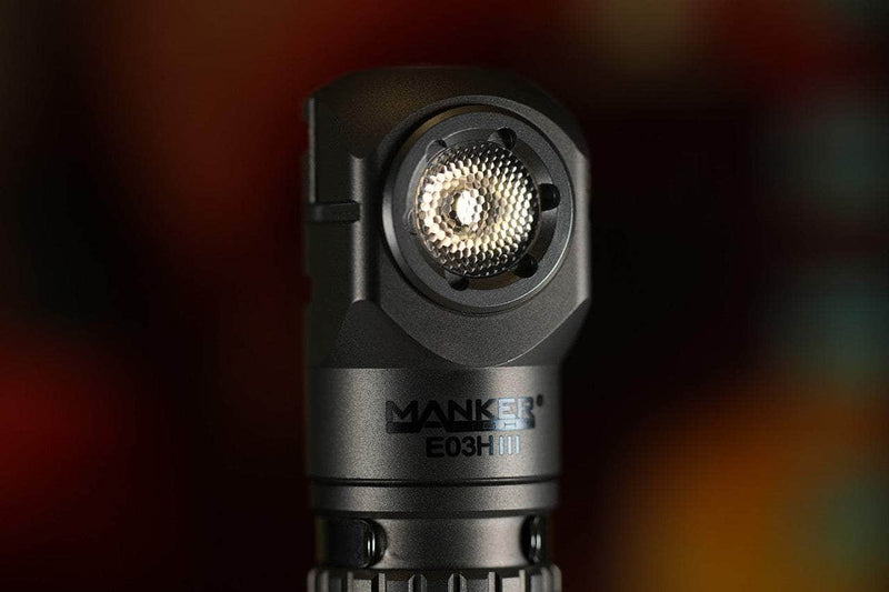 Close-up of a Manker E03H III - Titanium flashlight, highlighting its 1200-lumen LED and textured lens with a blurred background.