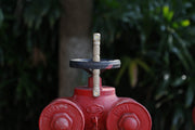 A close-up of a red outdoor water valve with two connections, surrounded by blurred green foliage in the background, illuminated by the Manker E03H III flashlight with 1200 lumens that highlights every detail.