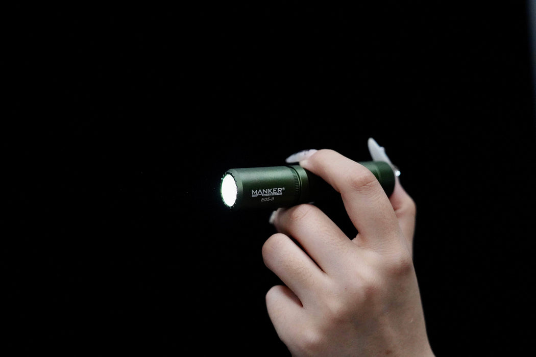 A person's hand holding a Manker E05 II flashlight.