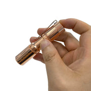 A person holding a compact Manker E05 II - Copper flashlight.