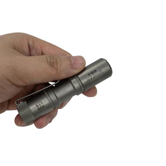 A person holding a Manker E05 II Ti flashlight on a white background.