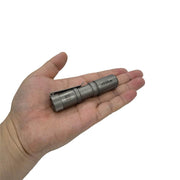 A hand holds the Manker E05 II Ti - Beadblasted, a compact titanium flashlight with a clip, ideal for everyday carry, shown against a white background.