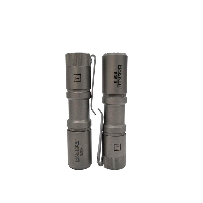 Two gray, cylindrical titanium Manker E05 II Ti flashlights with pocket clips stand upright side by side, each labeled "MAKER E561." Ideal for Everyday Carry, they deliver a powerful 1300 lumens of brightness.