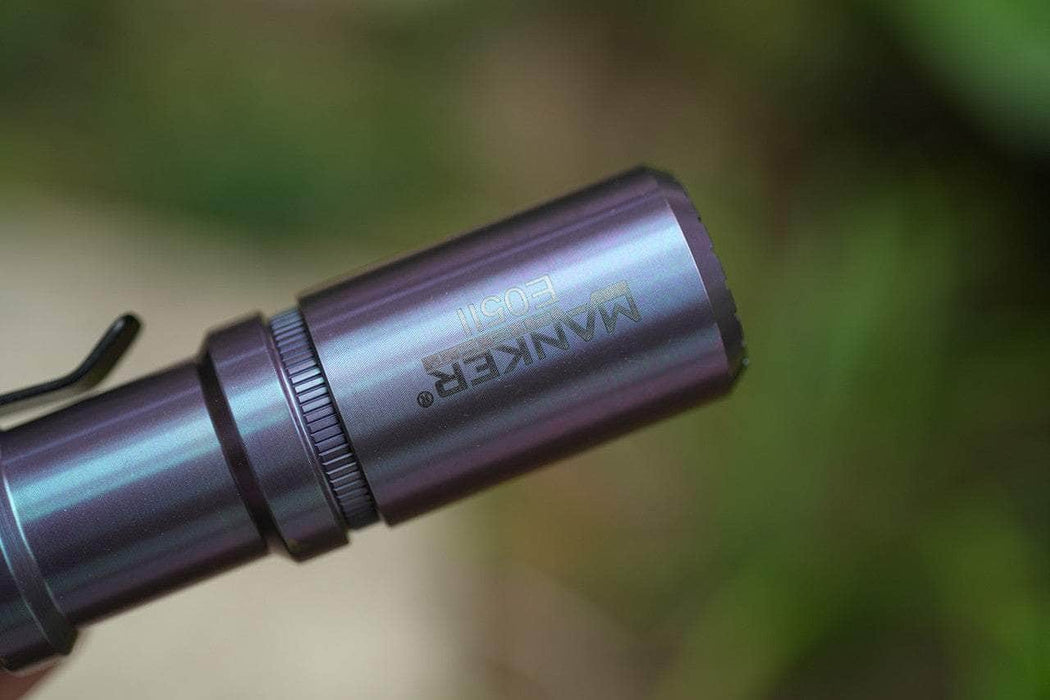 Close-up of the limited edition Manker E05 II Ti flashlight in Colorful MAO finish, with branding engraved on the side; ideal for everyday carry and photographed against a blurred green background.