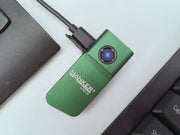 A green Manker LAD Mini Rechargeable Keychain Flashlight with a blue power button is connected to a USB-C charging cable, positioned between a laptop and a keyboard.