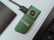 A green Manker LAD Mini Rechargeable Keychain Flashlight charges via USB-C next to a keyboard, with its red indicator light glowing.