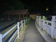 A paved pathway between a white fence and stone railing leads to illuminated wooden and tan structures at night—ideal for navigation using the Manker LAD Mini Rechargeable Keychain Flashlight with USB-C charging.