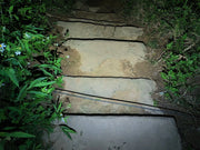 Stone steps surrounded by green plants, with a thin cable across them, illuminated at night by the Manker LAD Mini Rechargeable Keychain Flashlight.