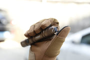 A gloved hand holds the Manker MC11 III USB-C Rechargeable Tactical Flashlight outdoors, with the thumb on the tail switch.