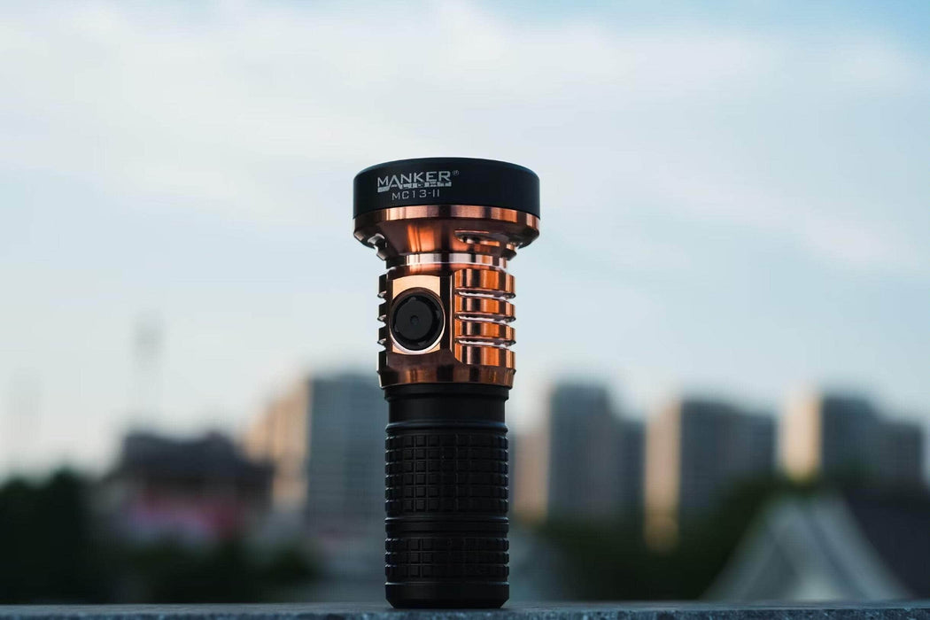 A Manker MC13 II - SBT90.2 Copper/Black Limited Edition flashlight sitting on top of a concrete wall.