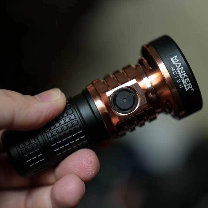 A person holding a Manker MC13 II - SBT90.2 Copper/Black Limited Edition camera with a red light.
