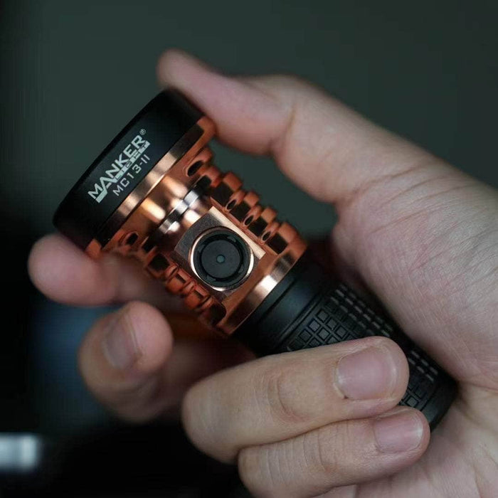 A person holding a Manker MC13 II - SBT90.2 Copper/Black Limited Edition with a small camera attached to it.