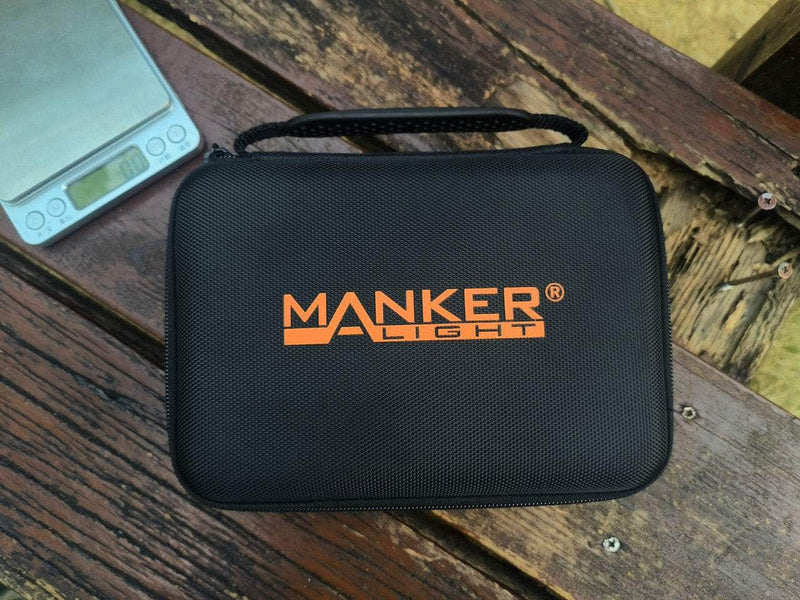 A Black Manker Ranger MK39 II carrying case sits on a wooden bench next to a digital scale reading "808," poised for action with its powerful spotlight capabilities.